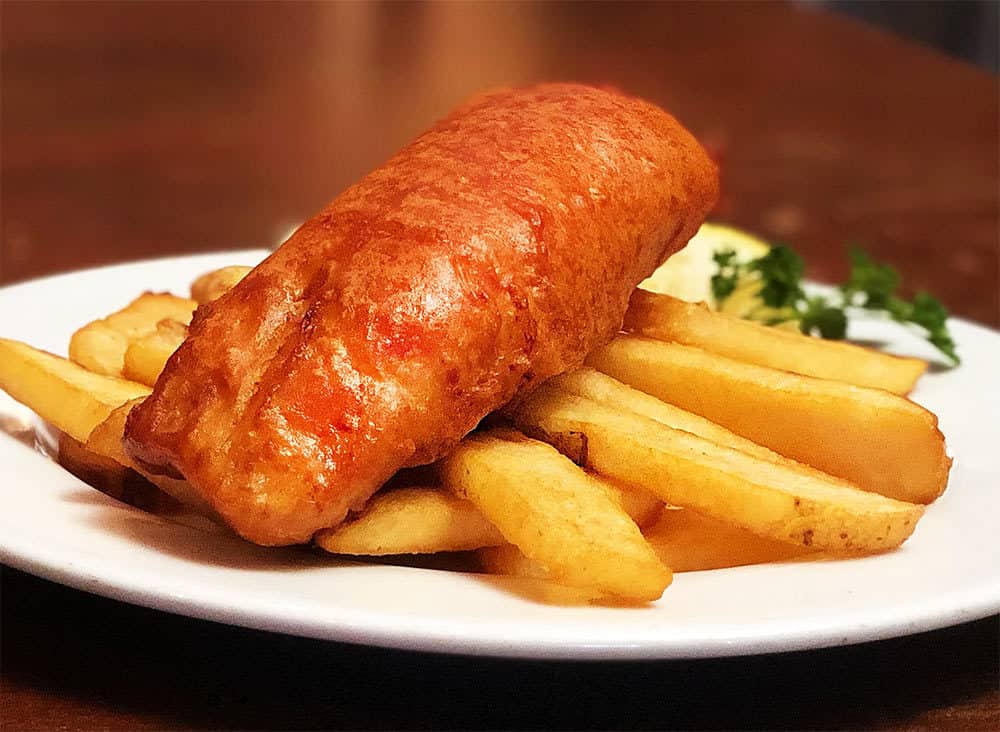 A large piece of creamy and fresh codfish, breaded and fried to perfection, sits on a pile of English "chips," or steak fries in the US. Delicious!