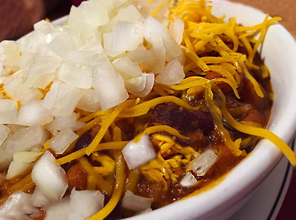 A big bowl of fresh chili topped with grated cheddar cheese and chopped onion