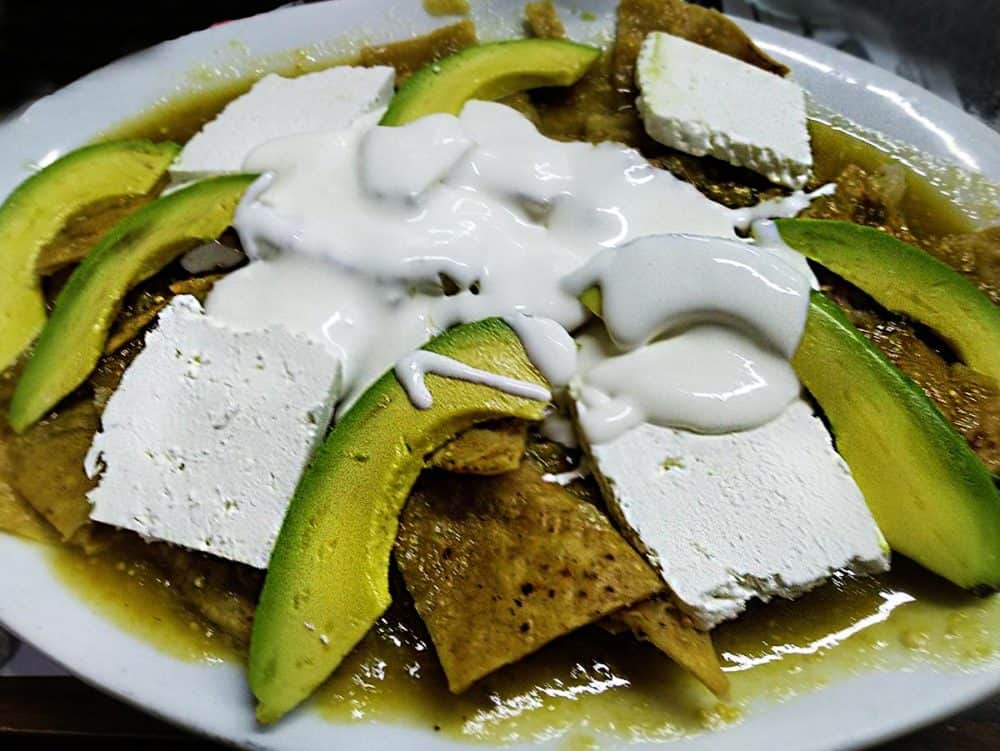 A delicious plate of traditional Mexican chilaquiles, made from crispy tortilla chips topped with fresh farmer's cheese, avocado, salsa verde, and sour cream. Yum!