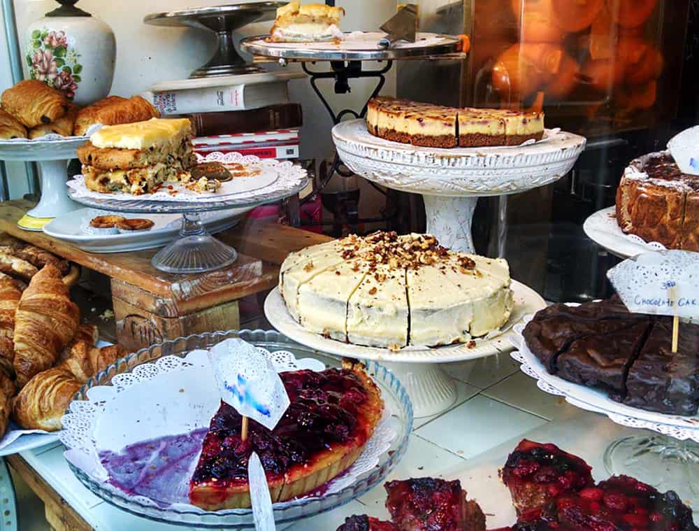 The fron window of De Laatste Kruimel is stacked high with vintage cake plates full of cakes and pies, cheesecake, brownies, and more.