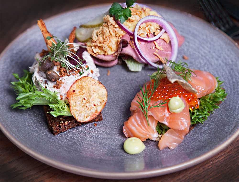 A plate of three Danish smørrebrød from Restaurant Maven in Copenhagen: Icelandic salmon with fennel, beef with horseradish and crisp fried onions, and chicken salad with capers.