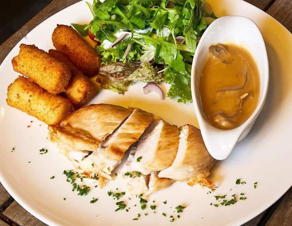 A plate of chicken breast with lightly crusted cheese croquettes, mushroom gravy, and a salad.